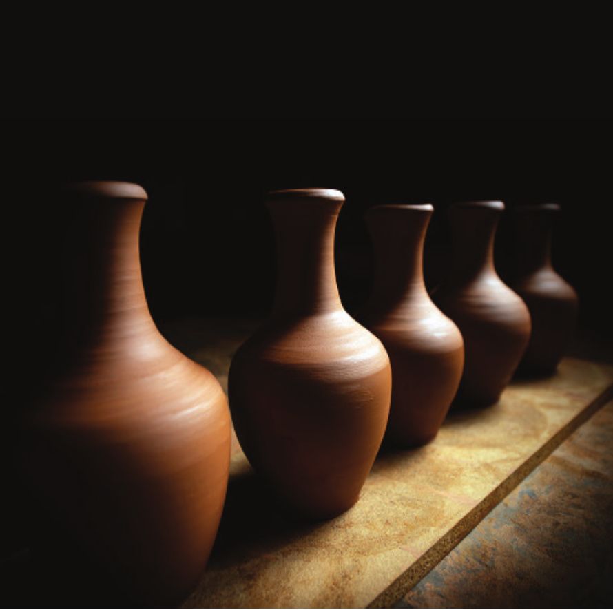 A row of terracotta vases lit from the side against a dark background