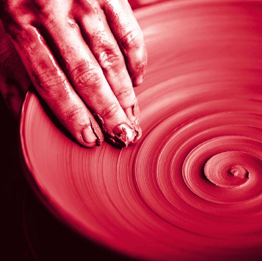 A hand pressing spiral grooves into red clay on a spinning wheel